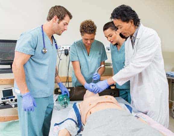 Four medical professionals practicing CPR techniques on a manikin during a training session.